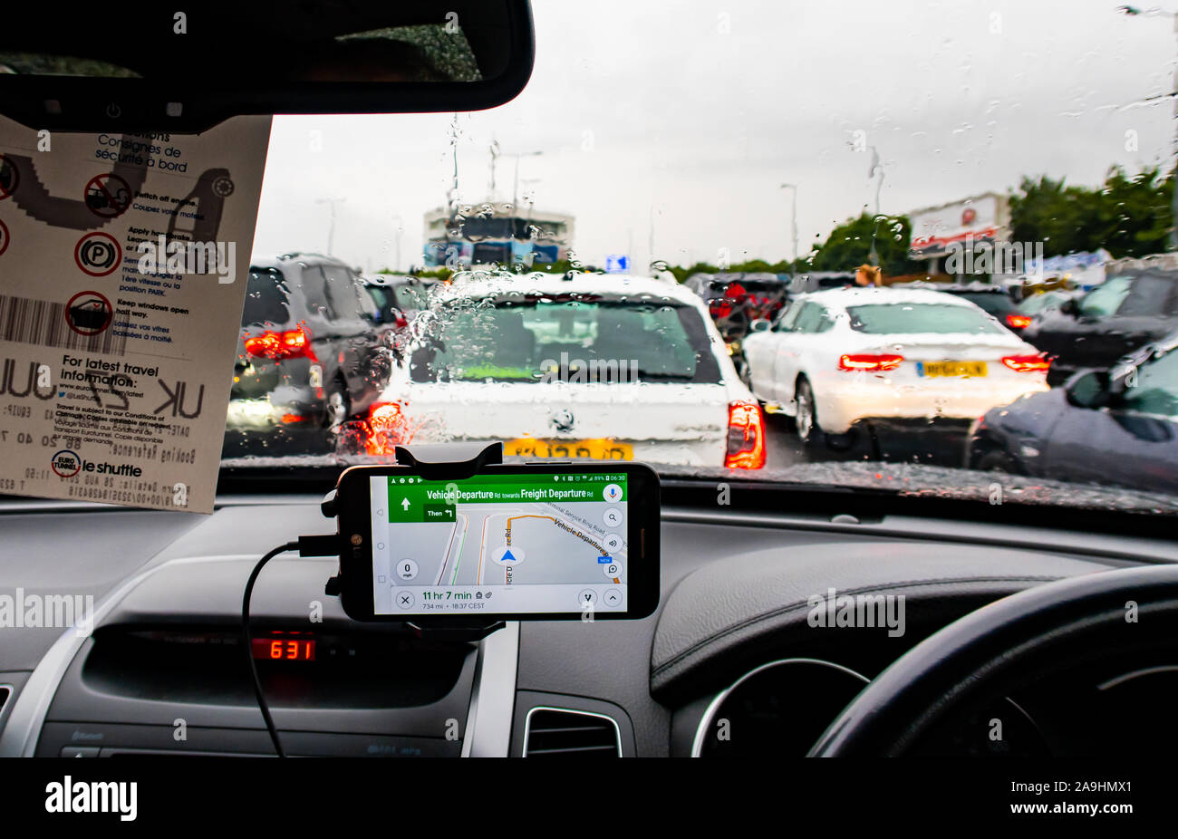 View from inside a car waiting for the shuttle at the Channel Tunnel in Folkestone on a rainy day.  A GPS Sat nav application on a mobile phone shows Stock Photo