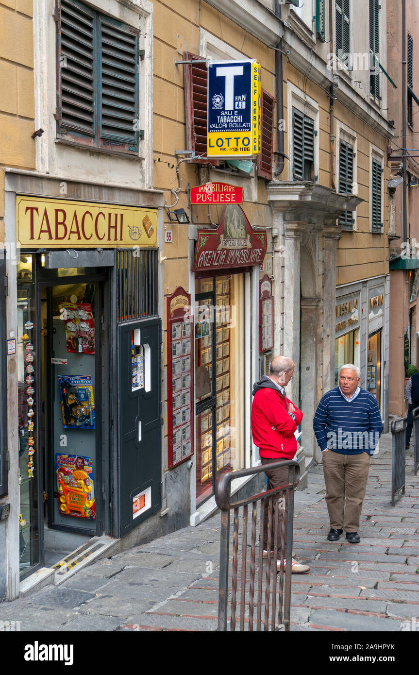 Two men talk on sidewalk outside tabacchi shop, Genoa, Italy Stock Photo