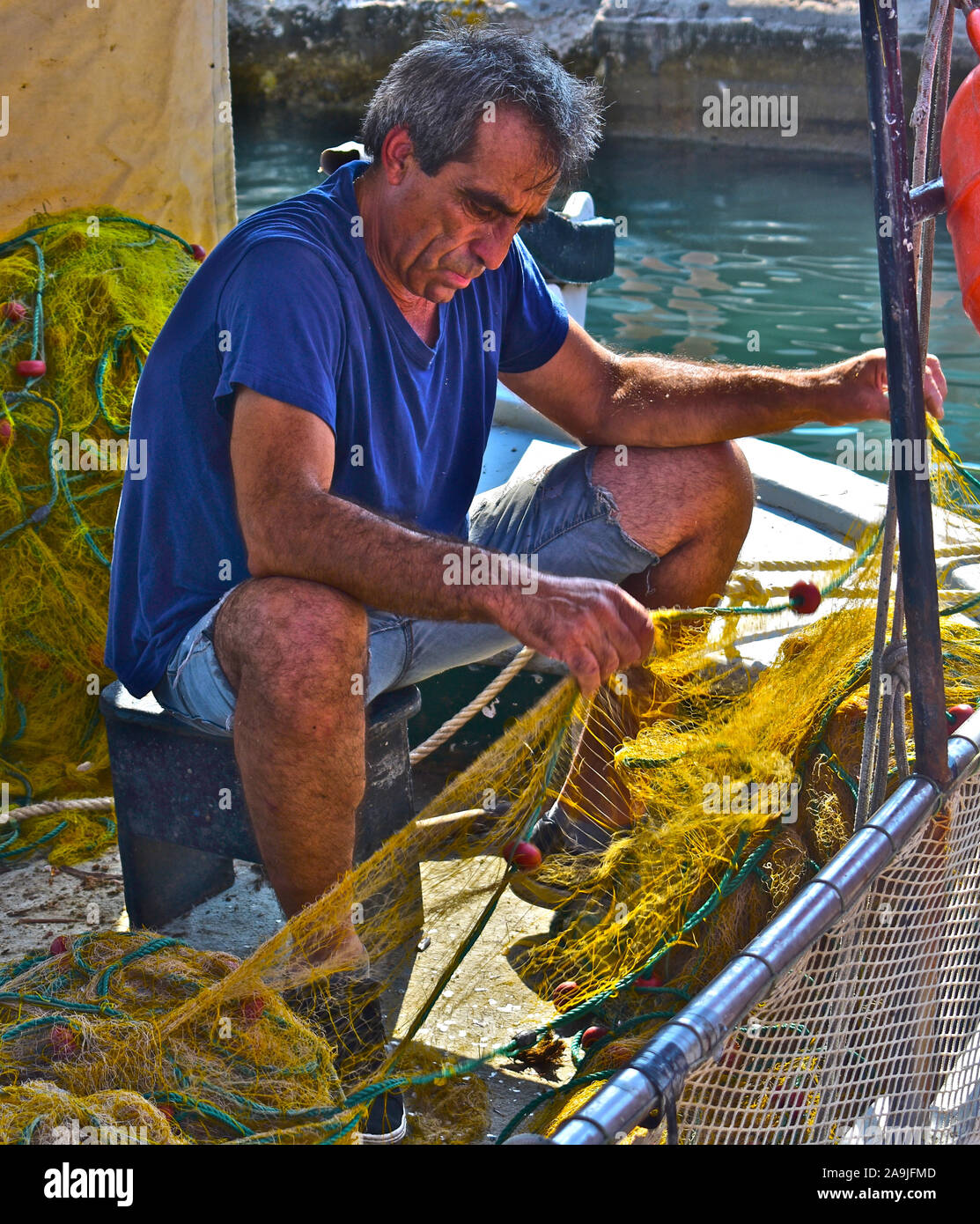 A typical Greek fisherman mending / cleaning nets aboard his small