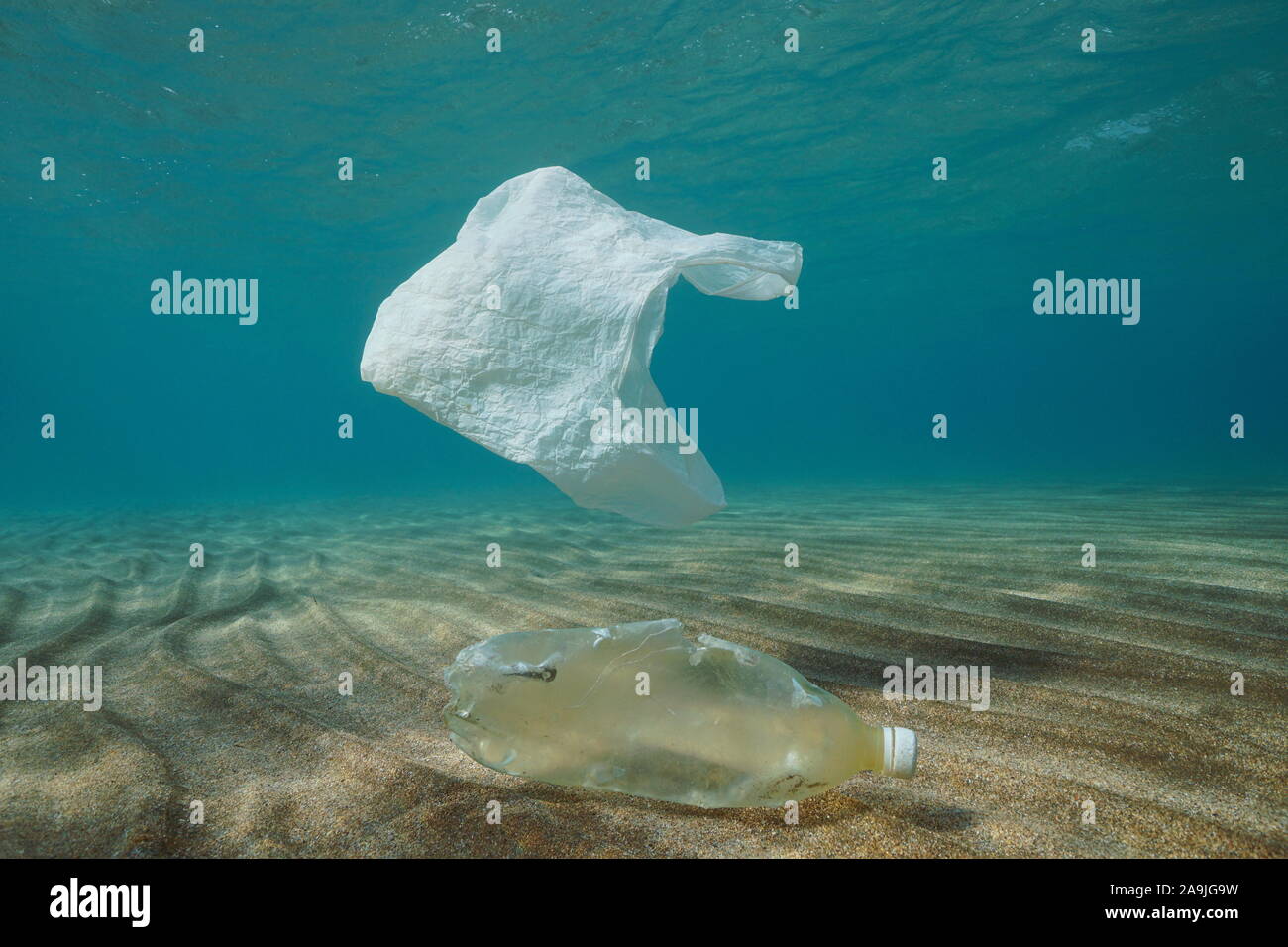 Plastic ocean pollution underwater, a plastic bag adrift and a bottle on a sandy bottom Stock Photo