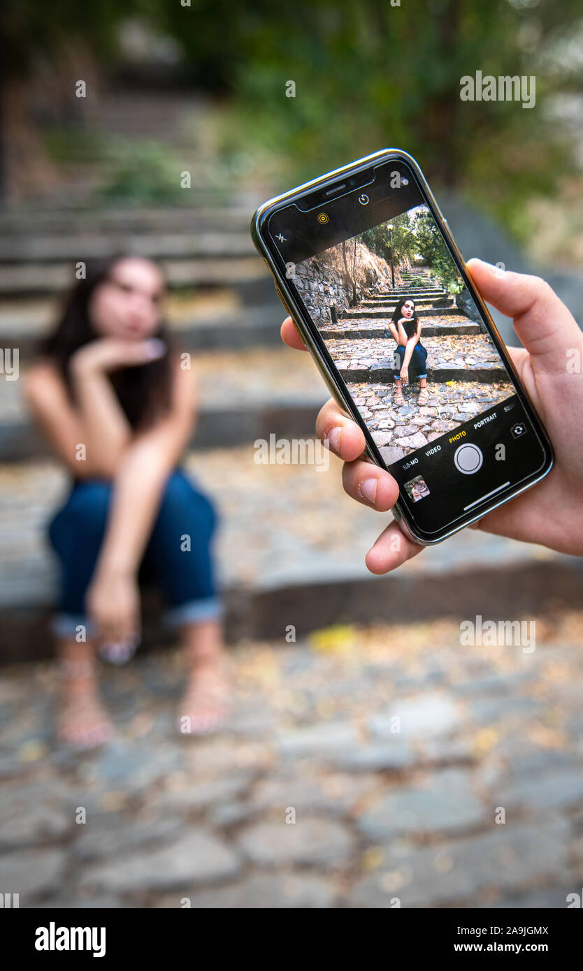Photographer taking photos of the young attractive girl using a mobile smartphone. Stock Photo