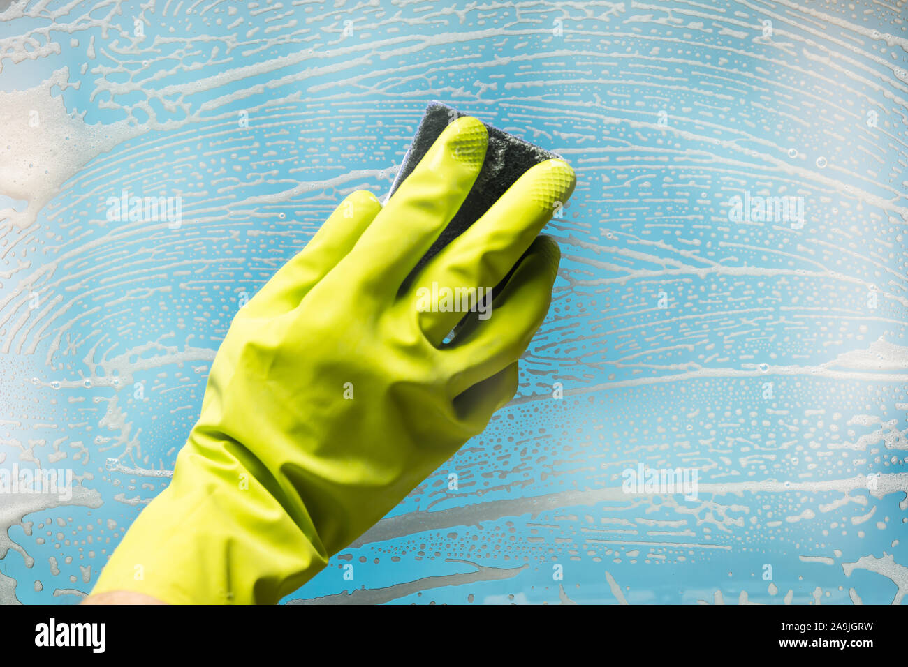 Person Wearing Green Gloves Cleaning Soap Suds Over Glass Window With Sponge Stock Photo