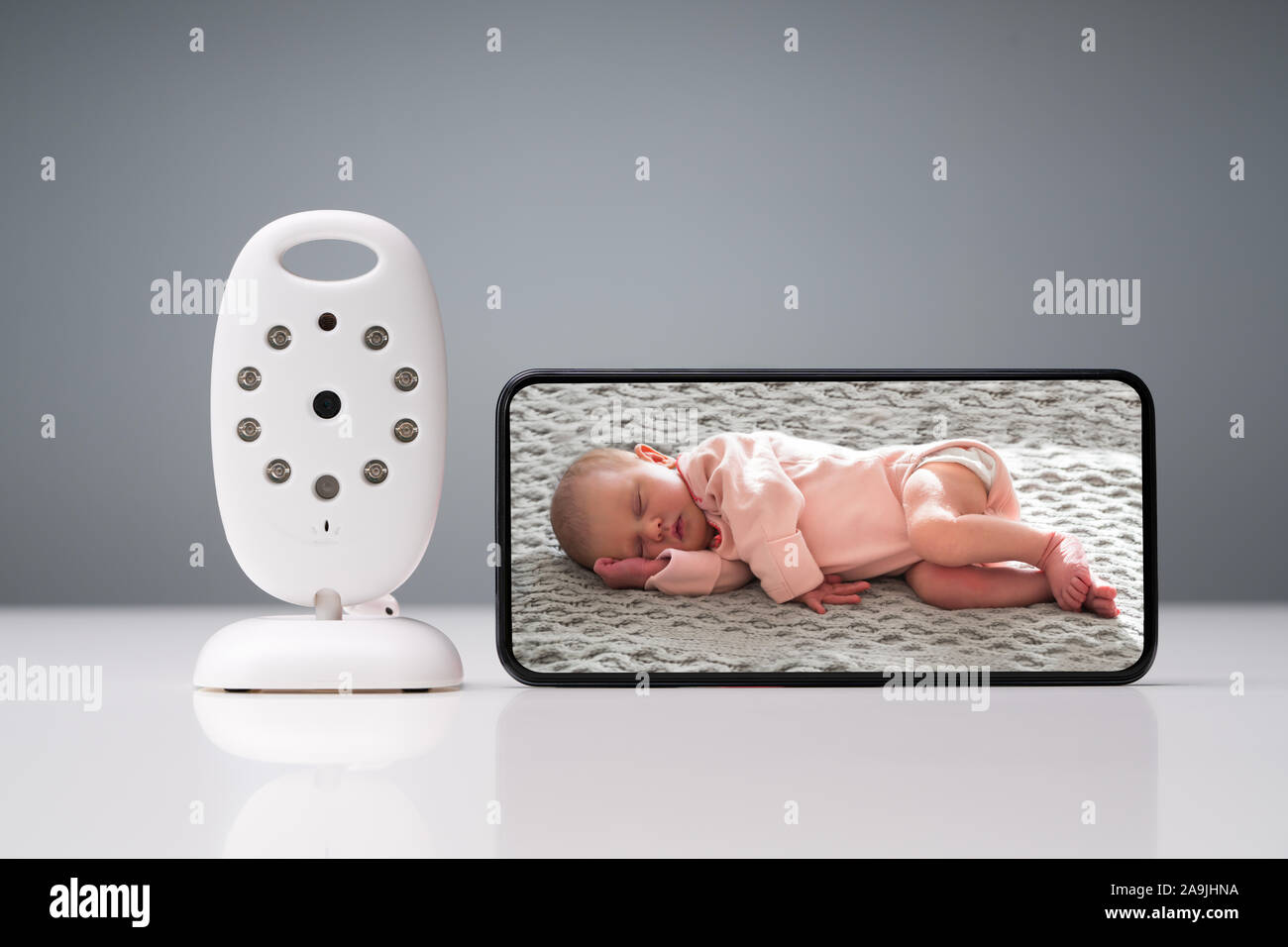 Close-up Of Wireless Camera And Smartphone With Baby Image On Screen On Reflective Table Stock Photo