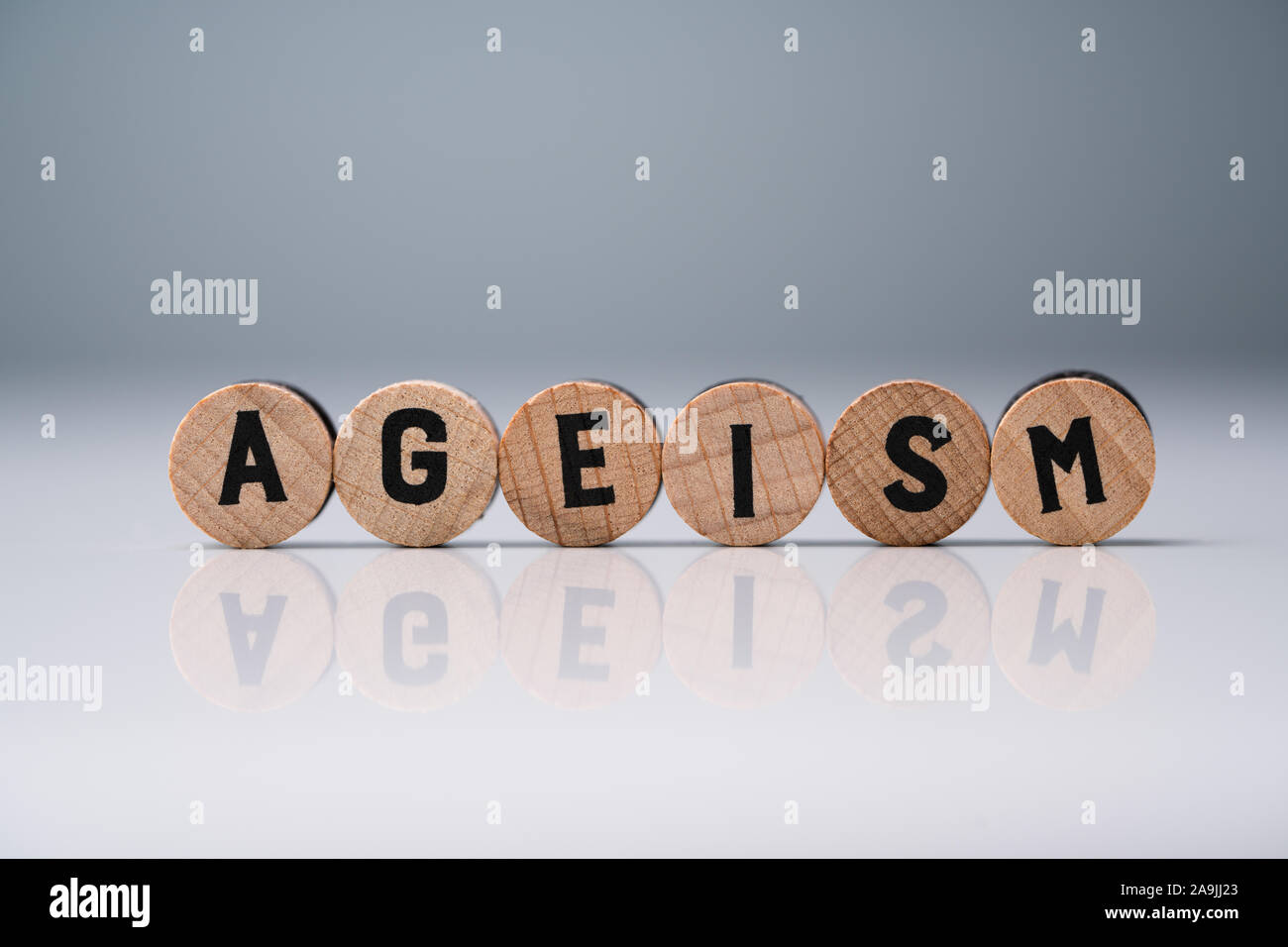 Ageism Text On Round Wooden Blocks Over Reflective White Desk Stock Photo