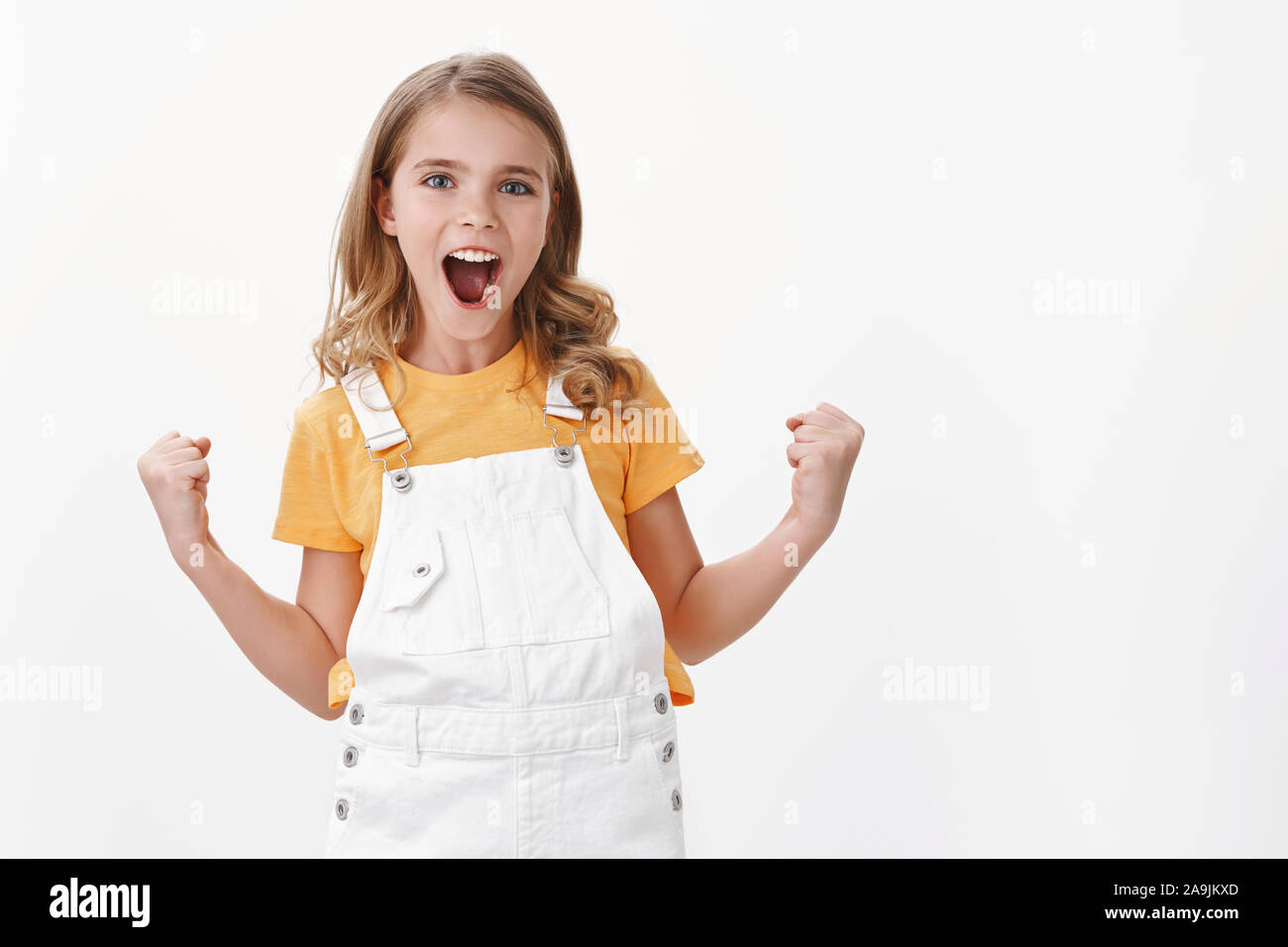 Proud good-looking young satisfied little girl with fair hair and blue eyes, fist pump celebration gesture, smiling joyfully, achieve success, triumph Stock Photo