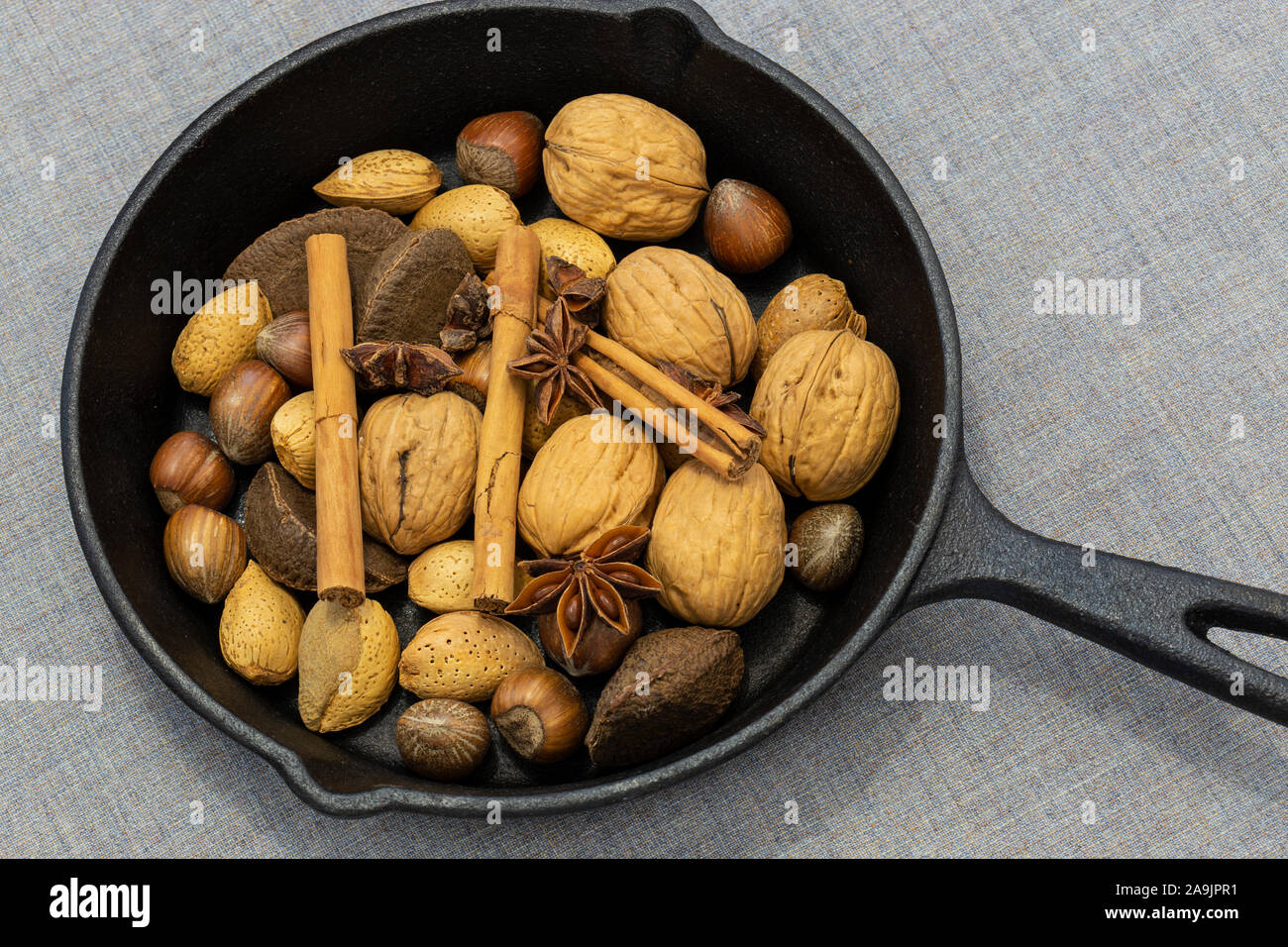 Walnuts, hazelnuts, Brazil nuts and walnuts in a cast iron frying pan with cinnamon sticks and star anise.  On a grey tablecloth Stock Photo