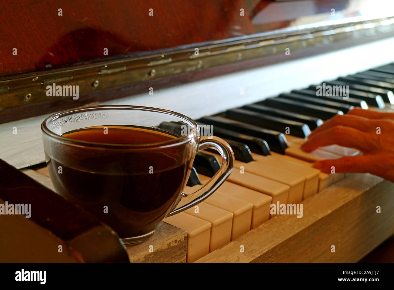 Cup of hot coffee on the piano with blurry pianist's hand in background Stock Photo