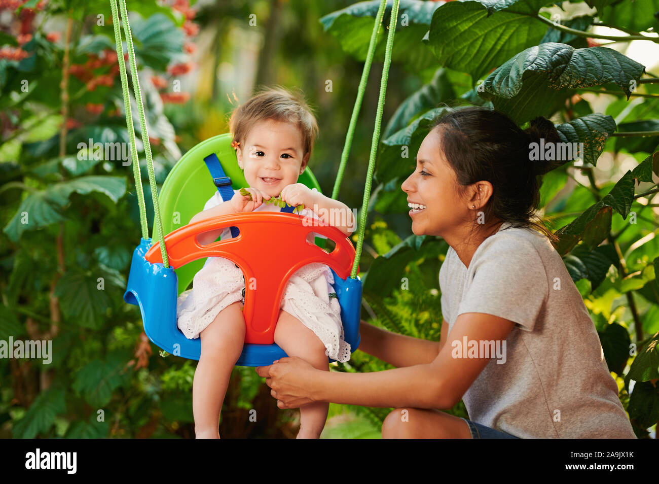 Mom with daughter play with swings on garden background Stock Photo