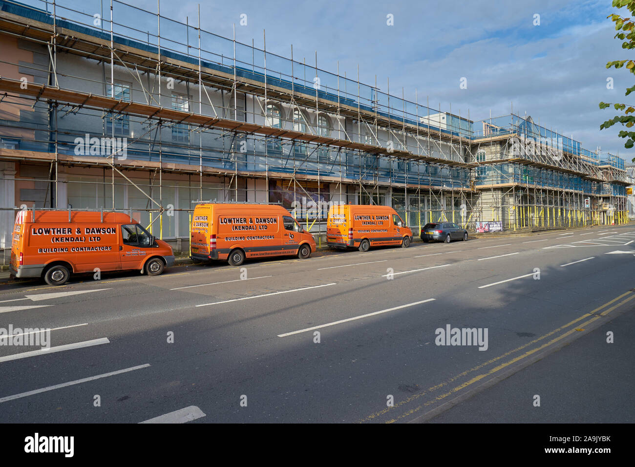 3 orange builders vans outside of the scaffolded K Village site in Kendal, Cumbria, UK during conversion to a Travel Lodge, a UK based hotel group Stock Photo