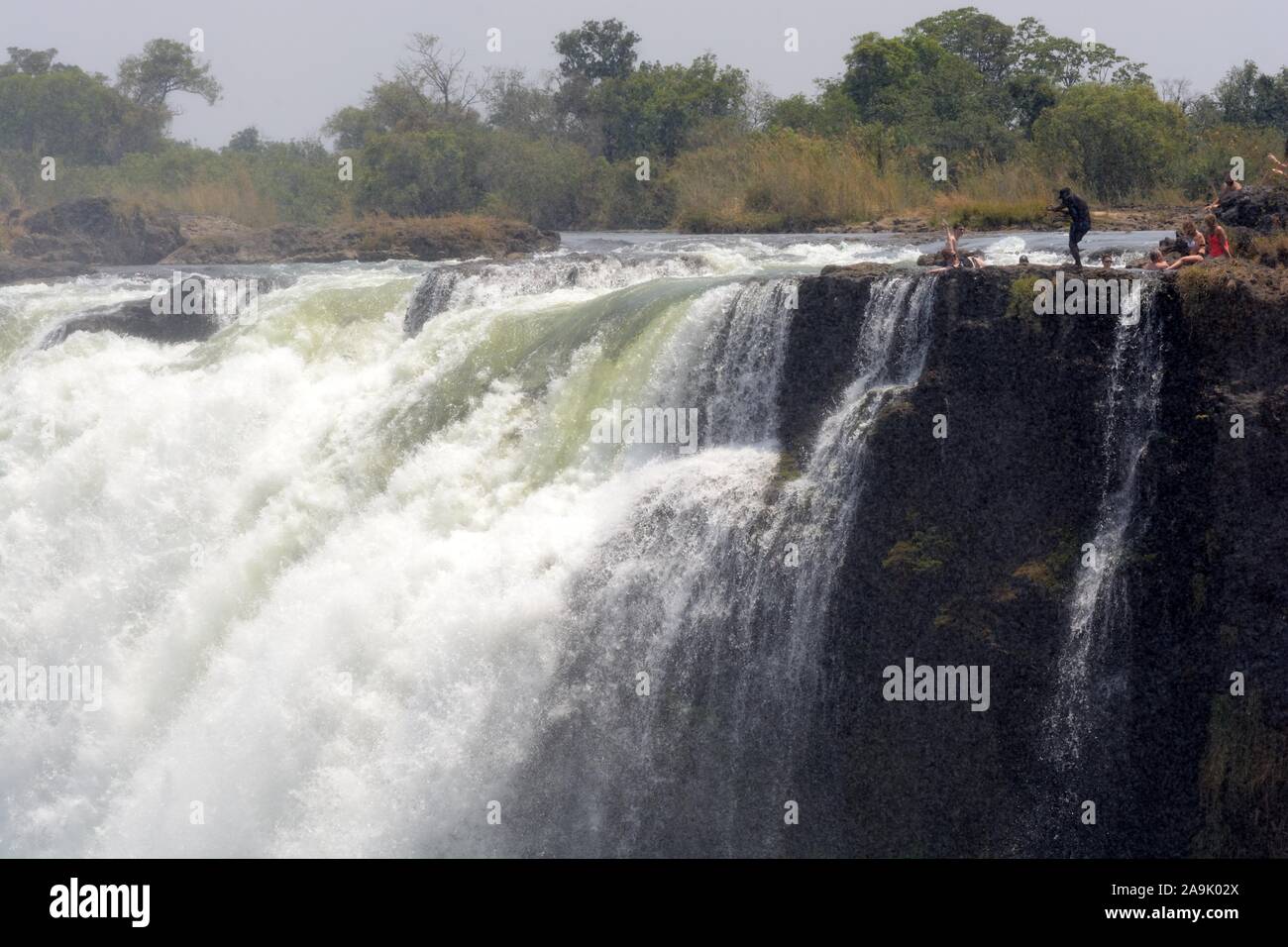 People tourists swimming in Devils Pool  on the edge of Victoria Falls Livingstone Island Zambia taken from the Zimbabwe side Africa Stock Photo