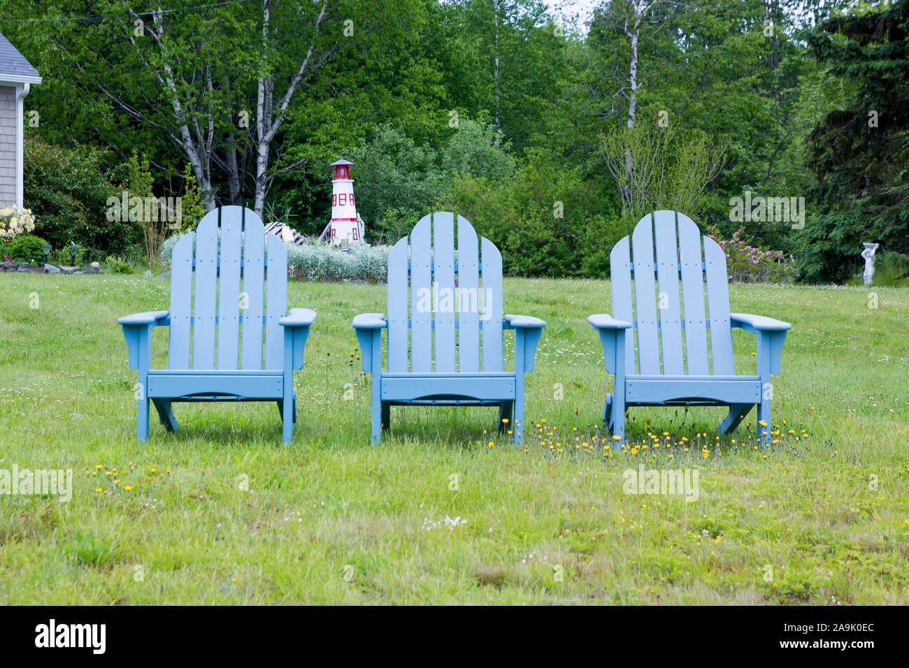 Three grey Adirondack chairs lined up on a lawn with a lighthouse sculpture in the background. In Maine, United States. Stock Photo