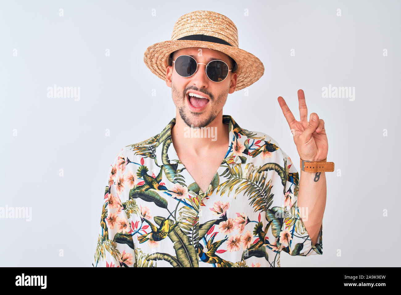 Young handsome man wearing Hawaiian shirt and summer hat over isolated ...