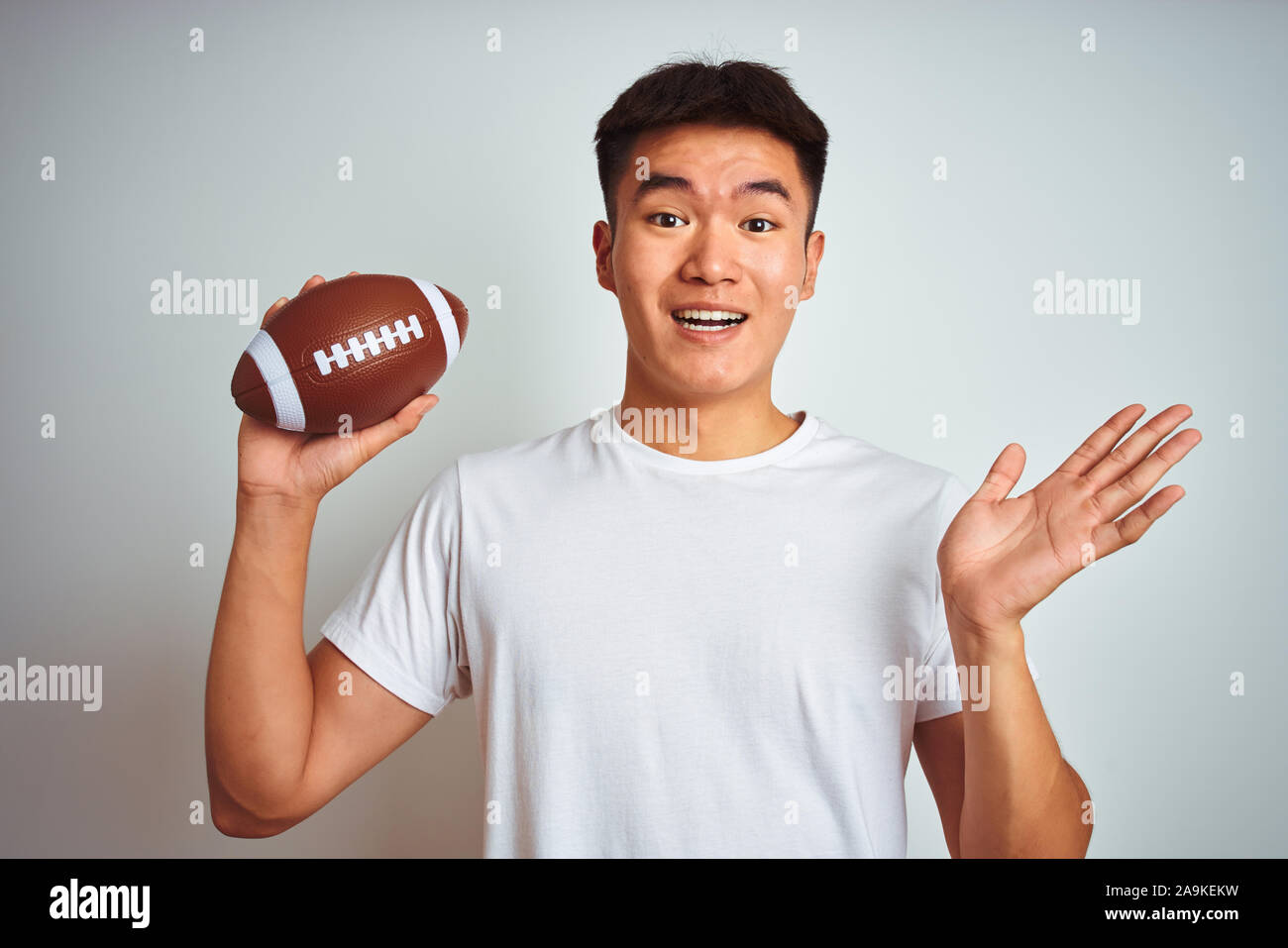 Young asian chinese sportsman holding rugby ball standing over isolated white background very happy and excited, winner expression celebrating victory Stock Photo