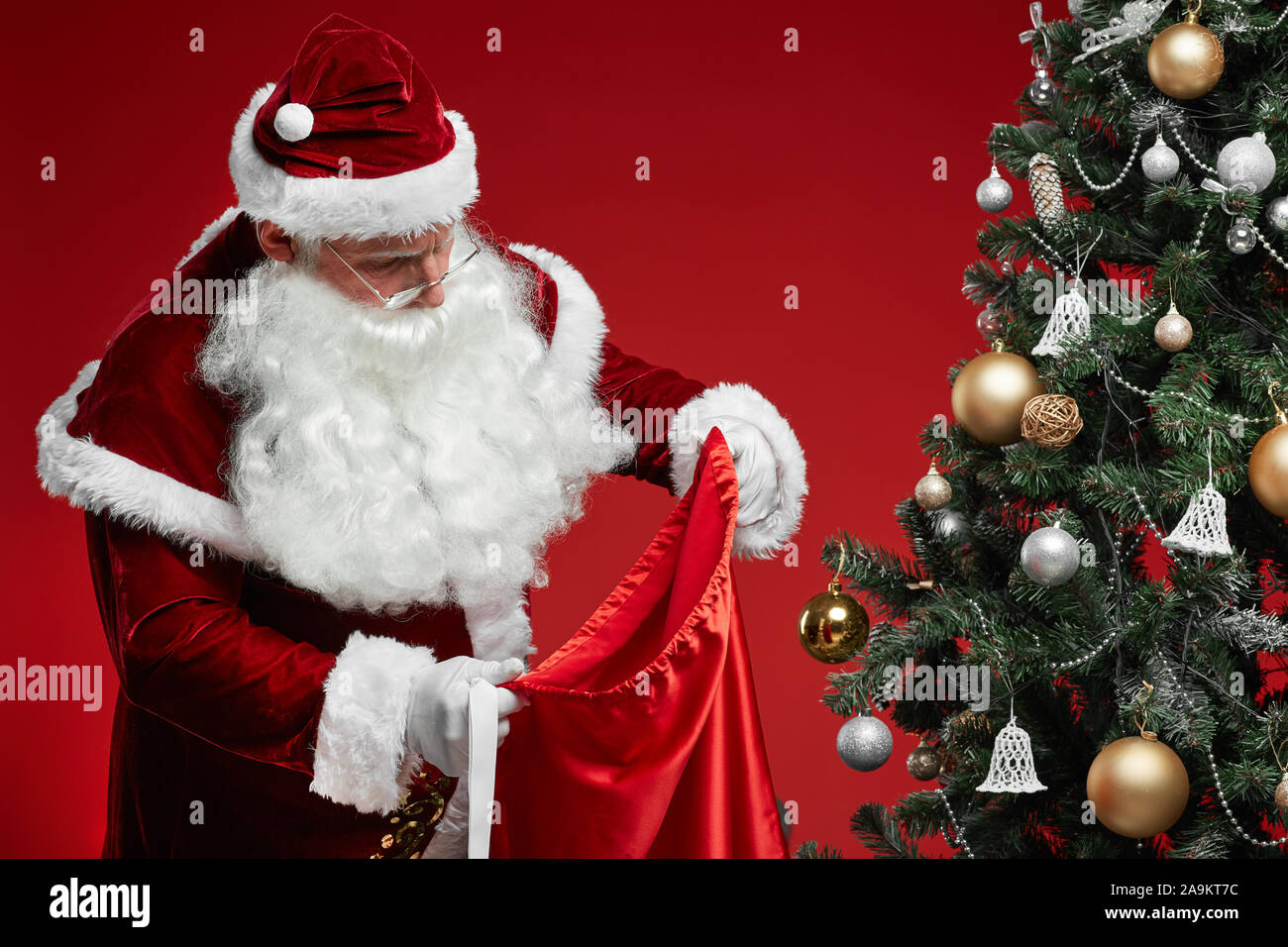 Santa Claus in red costume looking in his sack and preparing for the ...