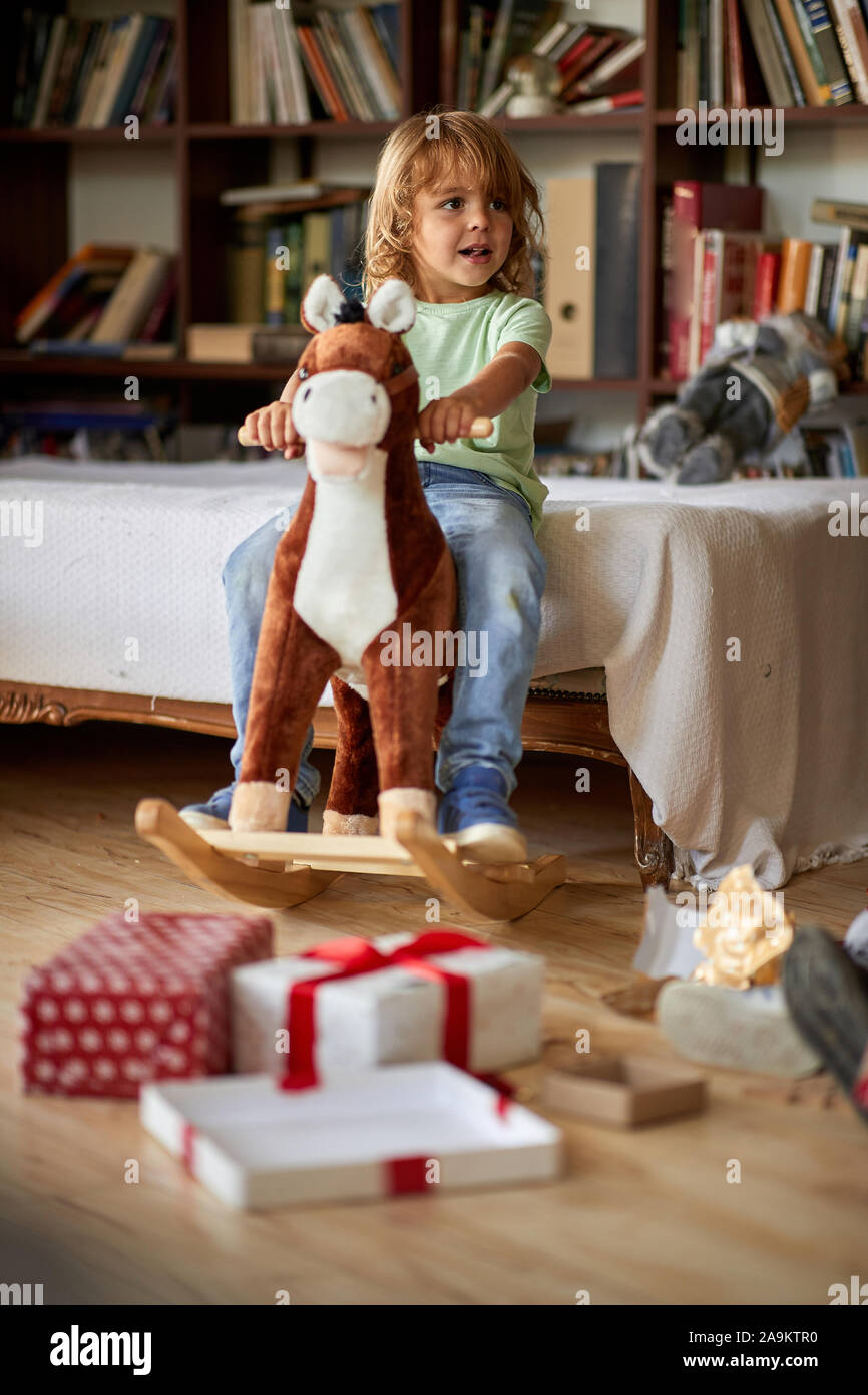 Small cute boy riding wooden rocking horse in front of christmas tree Stock Photo