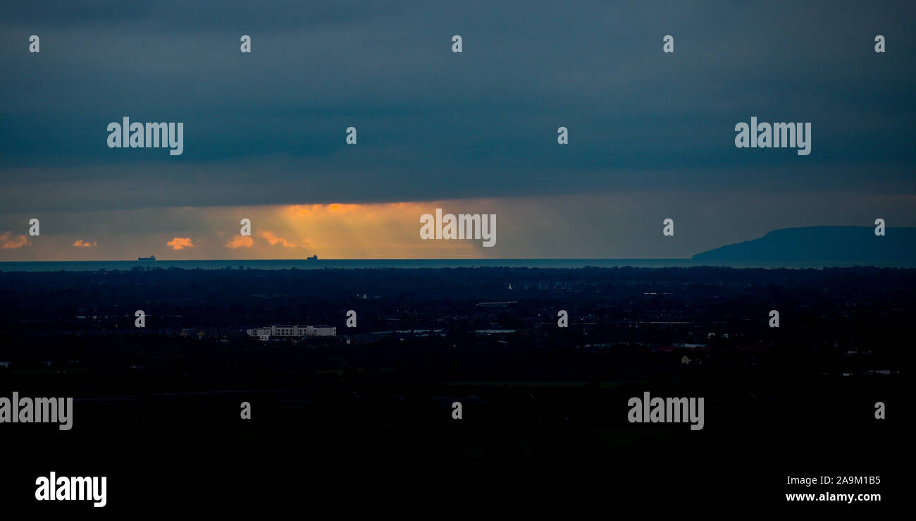 Chichester UK 16th November 2019 - A cargo ship is caught in a shaft of late afternoon sunshine in the English Channel just off the Isle of Wight coastline seen from  Halnaker near Chichester on a dull but dry afternoon in West Sussex . More unsettled weather with heavy rain is forecast for some parts of Britain over the next few days  : Credit Simon Dack / Alamy Live News Stock Photo