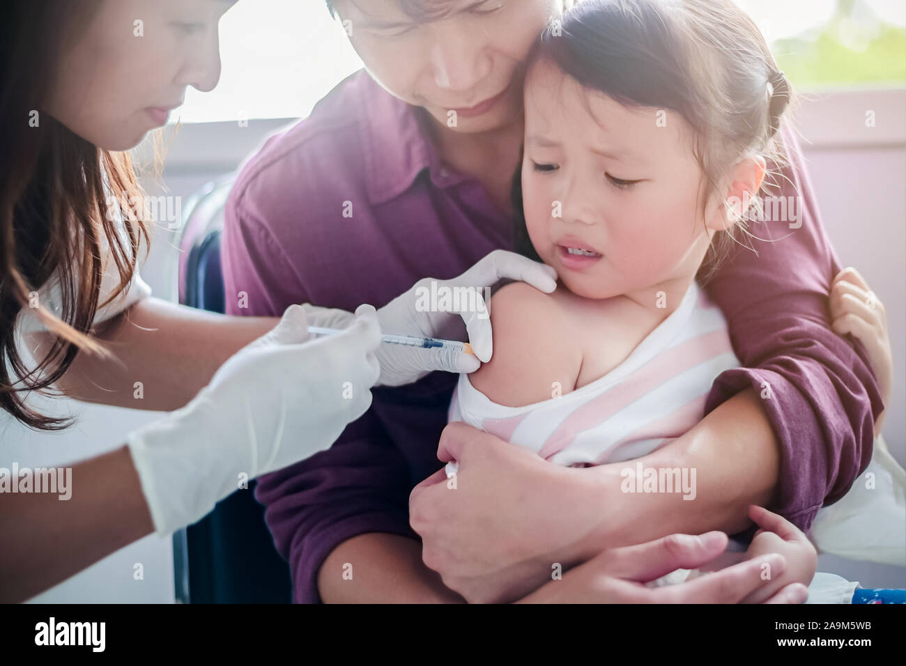 Little child having Injection,Close-up Doctor injecting vaccination to arm of asian little girl ,with the father hug the child, for not wriggle while Stock Photo
