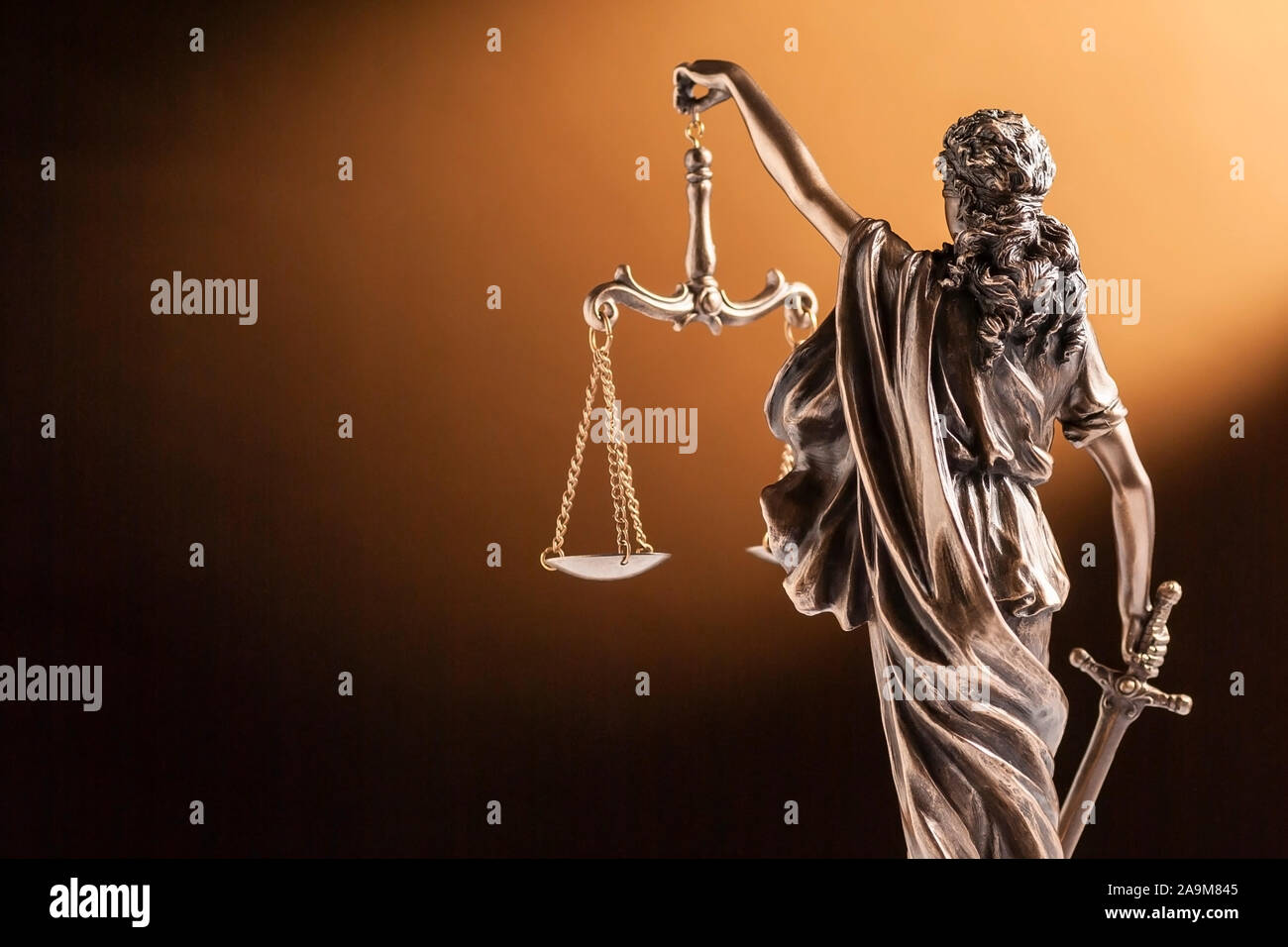 Rear view of of a small bronze figurine of Justice holding up the scales of law and order and carrying a sword facing towards blank copy space on brow Stock Photo