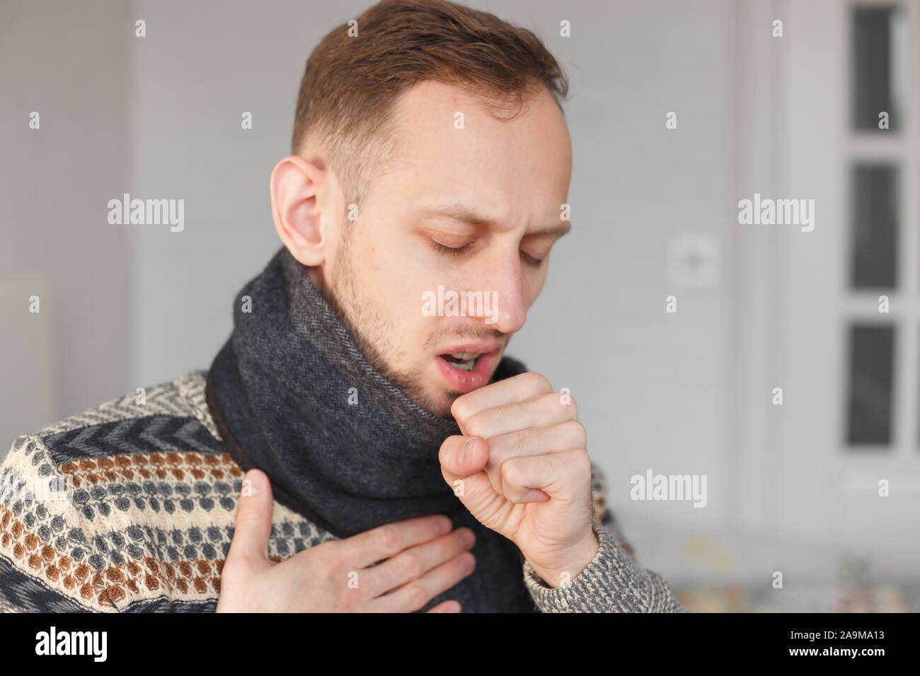 Young man with scarf on his neck is coughing because of cold and sore