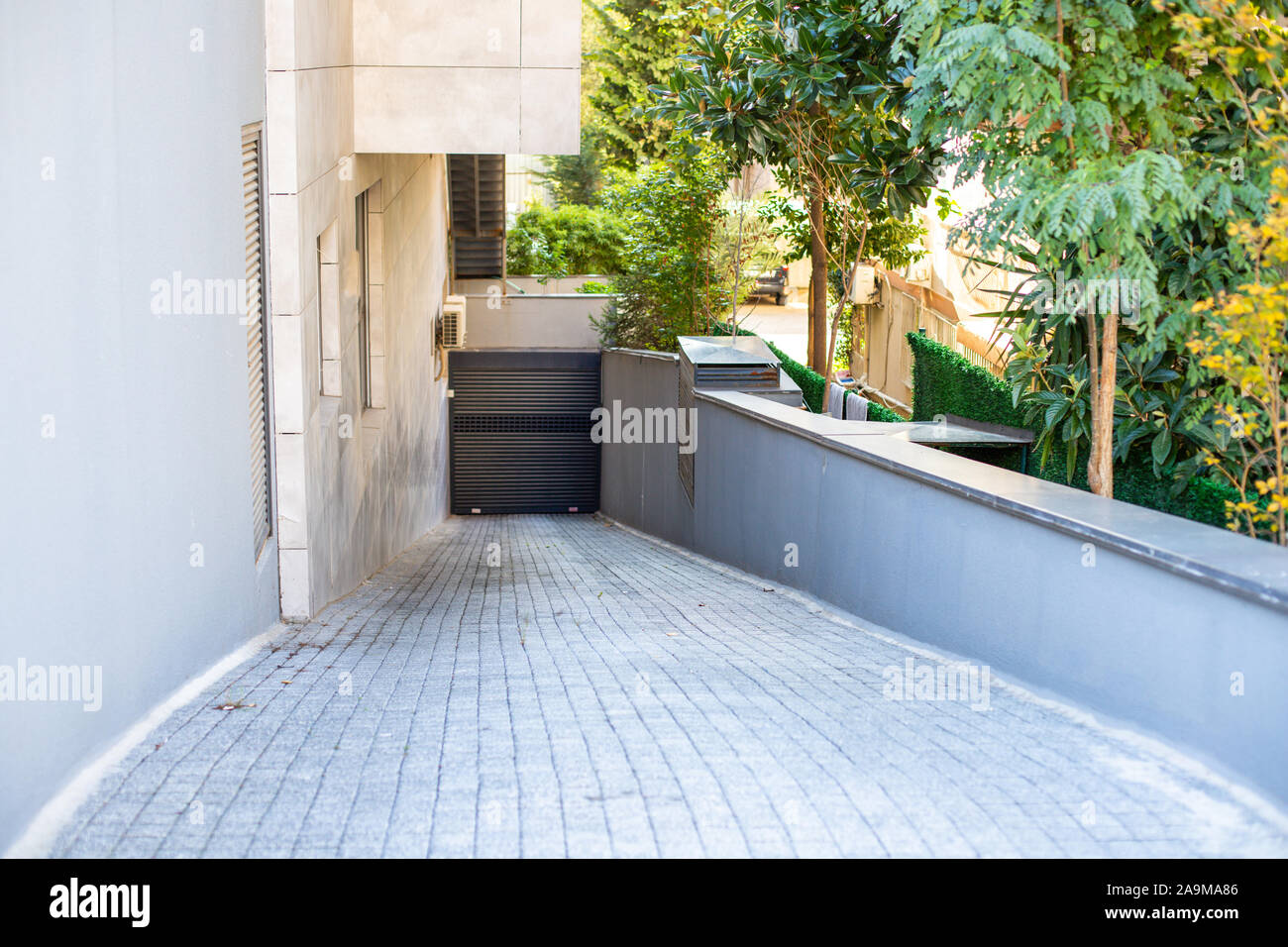 Steep paving descent to the parking lot. Automatic shutter Rolling gates. Residential complex with lots of greenery. Stock Photo
