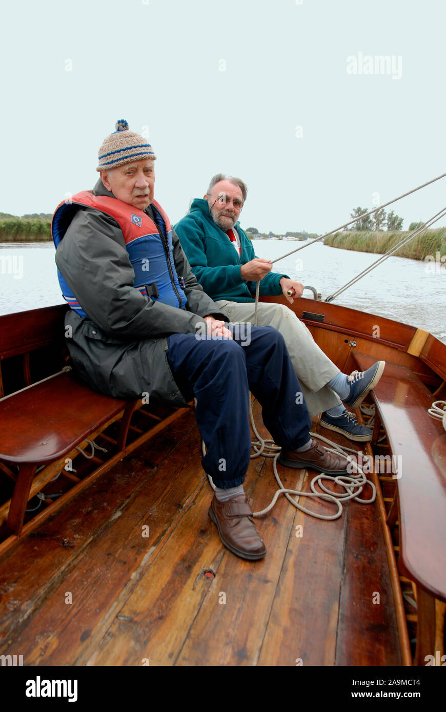 Two elderly men sailing a small open dinghy in inclement weather, Norfolk, England Stock Photo