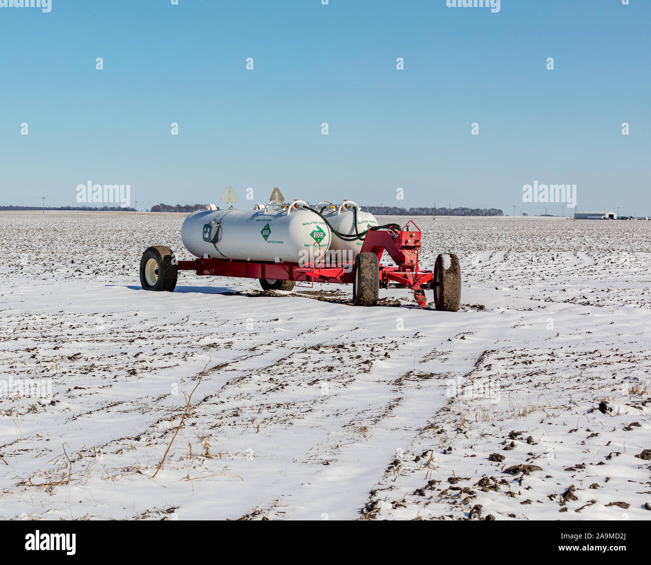 Anhydrous ammonia fertilizer tanks and wagon in harvested soybean farm field covered in snow after an early winter snowstorm Stock Photo