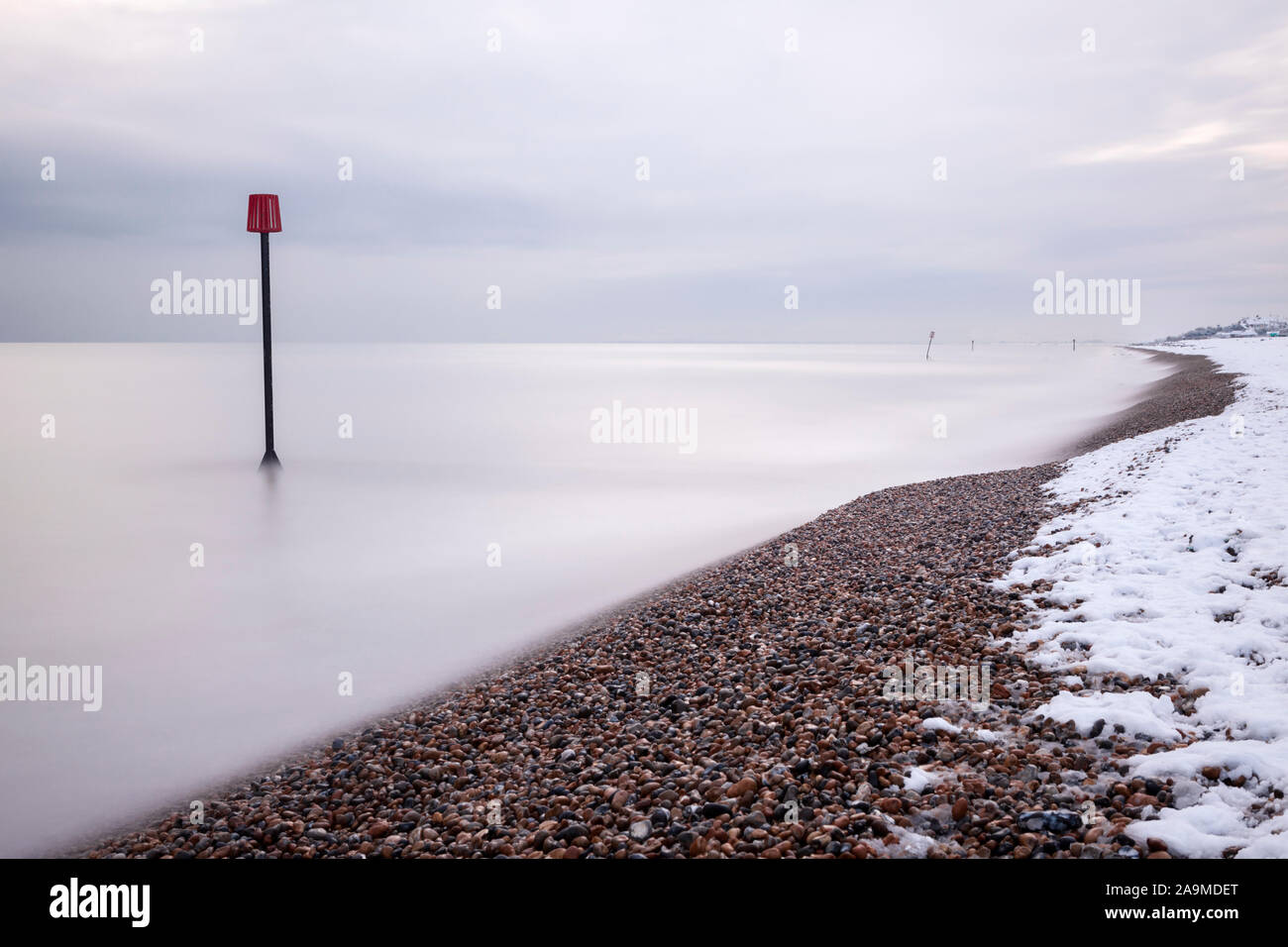 Groyne marker and snow covered beach at Bexhill on Sea, East Sussex, UK, long exposure Stock Photo