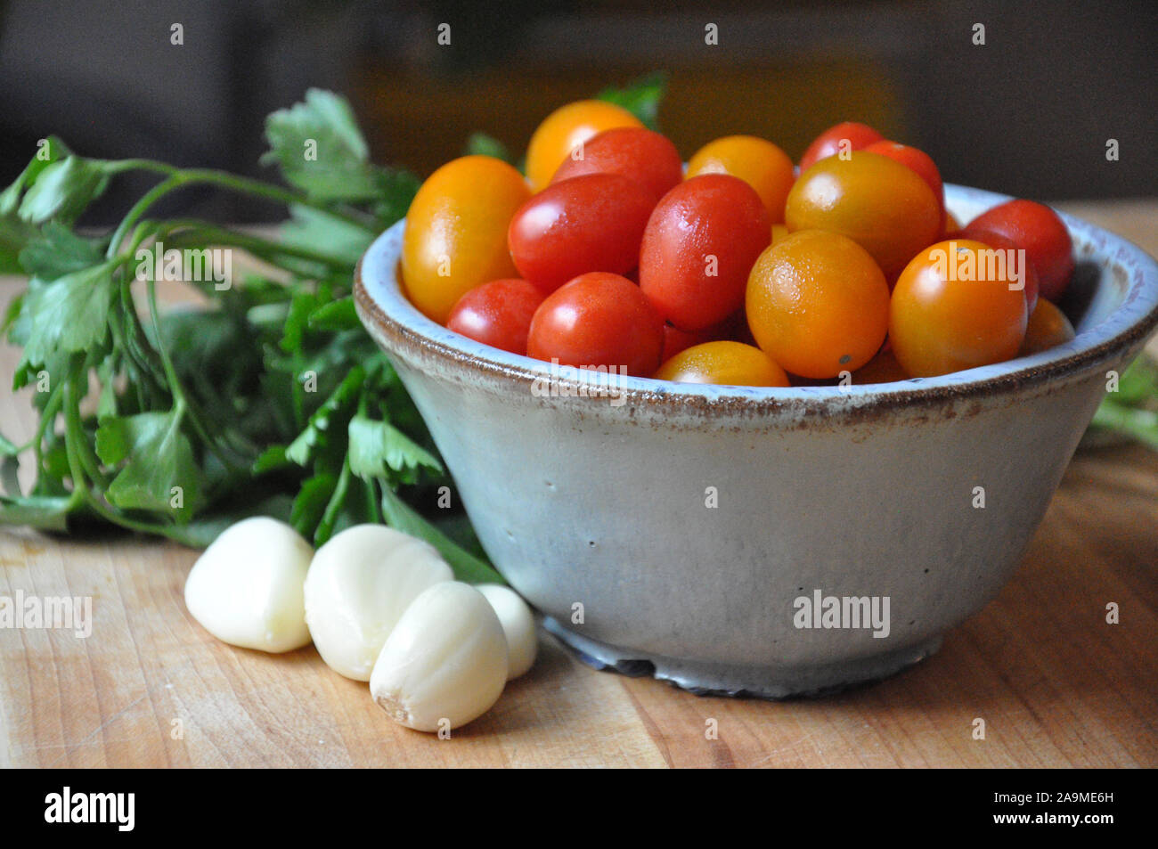 Cherry Tomatoes, garlic and parsley on a wooden cutting board Stock Photo