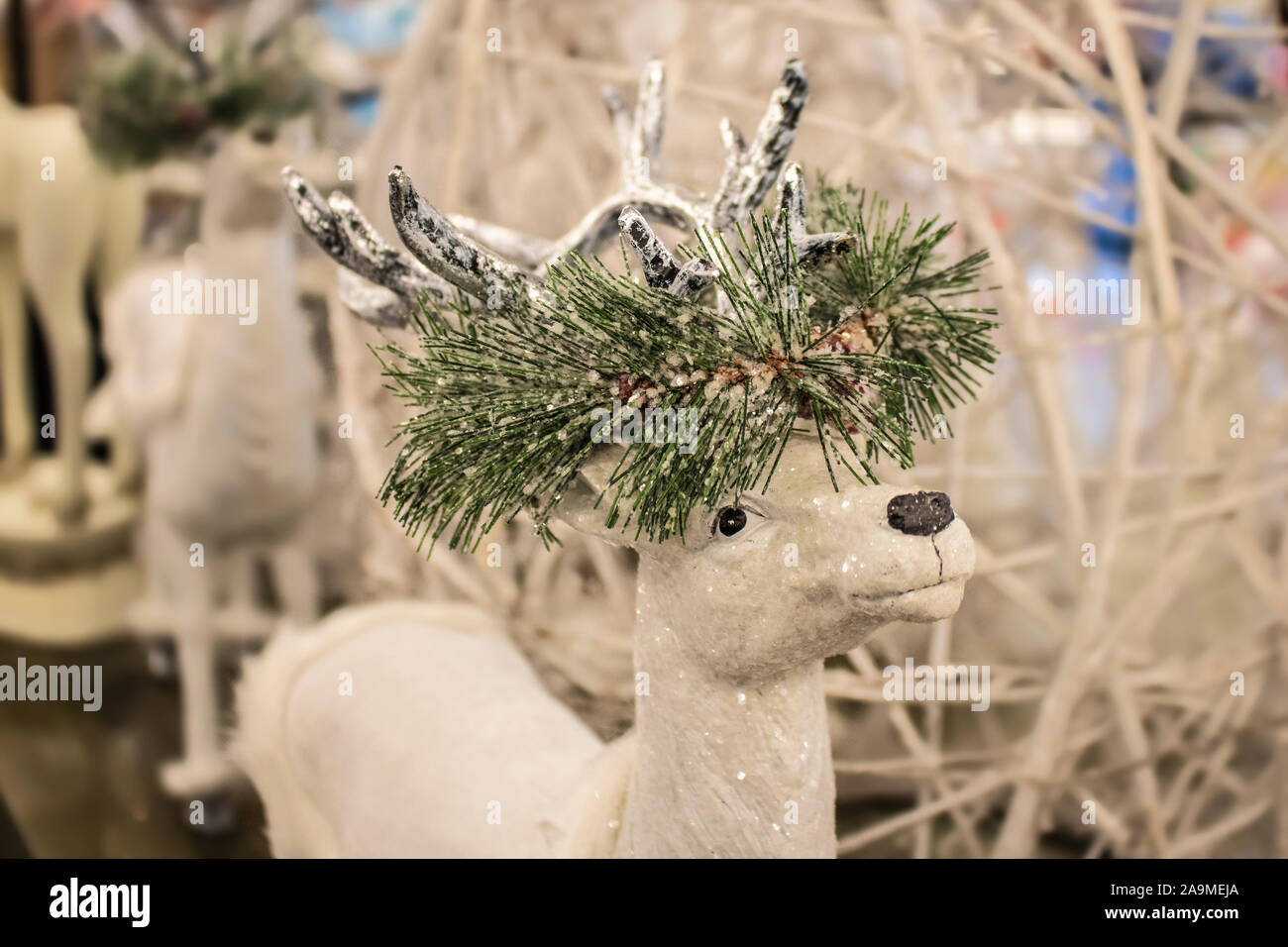 Close-up cropped white sparkly reindeer Christmas decoration with garland of snow covered greenery around horns - selective focus against blurred back Stock Photo