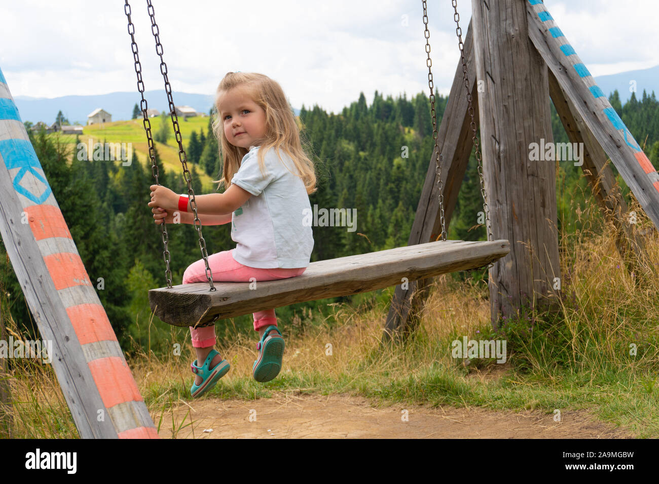 Little girl swinging on swing with mountain view on background Stock Photo