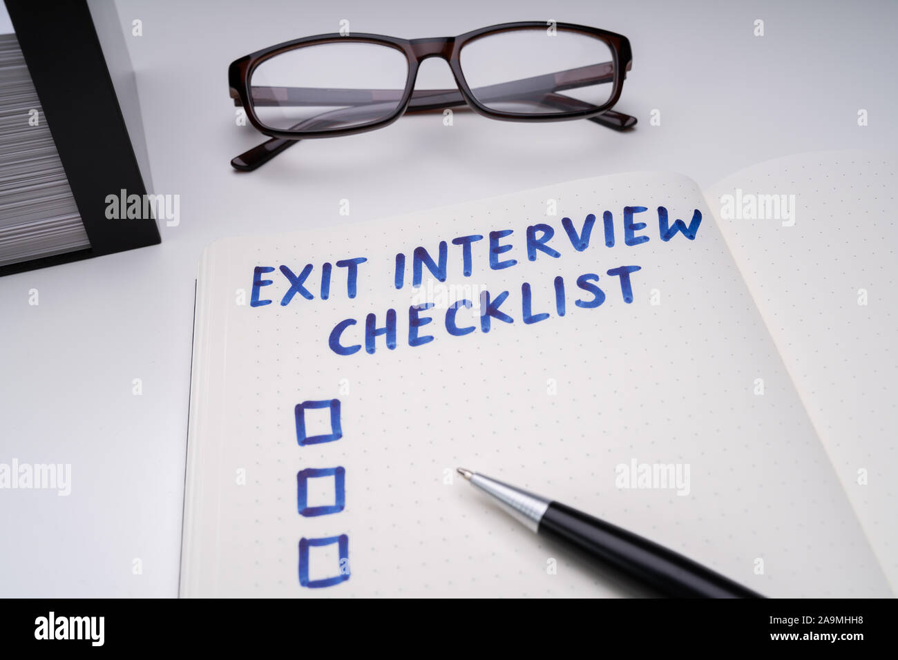 Handwritten Exit Interview Checklist Message On Notebook With Blue Marker And Spectacles Over Office Desk Stock Photo