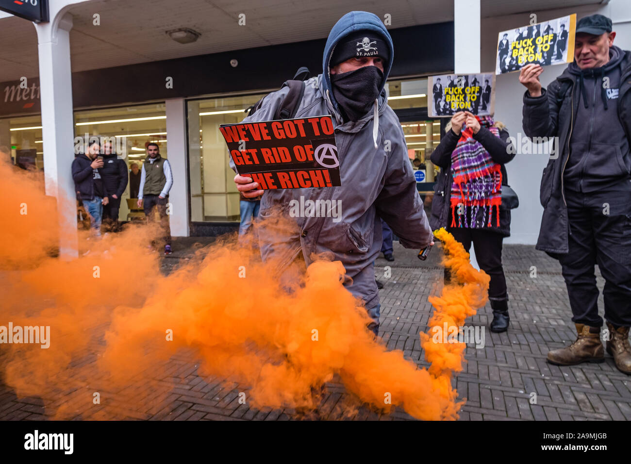 London, UK. 16th November 2019. Anarchists join the protest saying 'Why Vote? Revolt!' and set off an orange flare  as FCKBoris in orange knitted hats walk through Uxbridge shopping centre handing out fliers urging everyone to register and vote against Boris Johnson and kick him out for his racist, elitist politics. They marched with a sound system on a bus to Brunel University to persuade students. Johnson had a majority of just over 5 thousand in 2017 and Labour candidate Ali Milani has strong hopes of beating him and the other 10 candidates. Peter Marshall/Alamy Live News Stock Photo