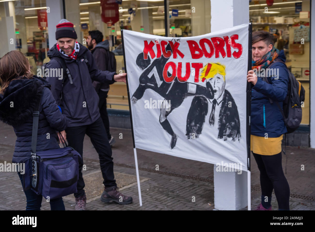 London, UK. 16th November 2019. KICK BORIS OUT banner. Protesters from FCKBoris in orange knitted hats walk through Uxbridge shopping centre handing out fliers urging everyone to register and vote against Boris Johnson and kick him out for his racist, elitist politics. They marched with a sound system on a bus to Brunel University to persuade students. Johnson had a majority of just over 5 thousand in 2017 and Labour candidate Ali Milani has strong hopes of beating him and the other 10 candidates. Peter Marshall/Alamy Live News Stock Photo