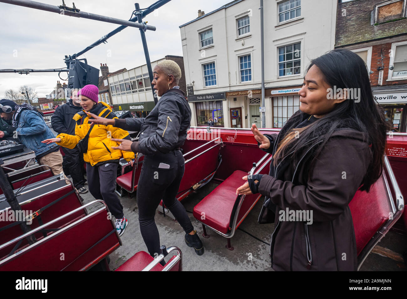 London, UK. 16th November 2019. People dance on top of the bus. Protesters from FCKBoris in orange knitted hats walk through Uxbridge shopping centre handing out fliers urging everyone to register and vote against Boris Johnson and kick him out for his racist, elitist politics. They marched with a sound system on a bus to Brunel University to persuade students. Johnson had a majority of just over 5 thousand in 2017 and Labour candidate Ali Milani has strong hopes of beating him and the other 10 candidates. Peter Marshall/Alamy Live News Stock Photo