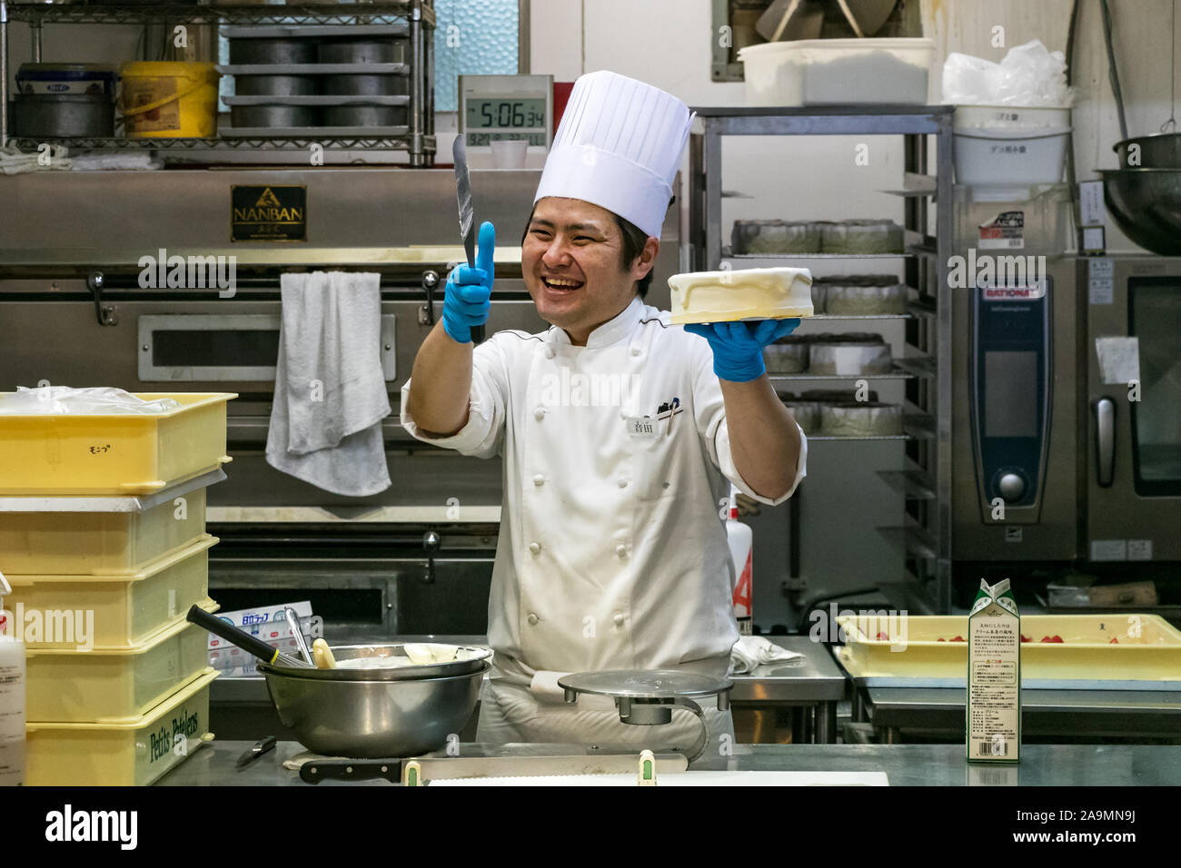 A Japanese male pastry chef smiling holding a round cake to decorate at