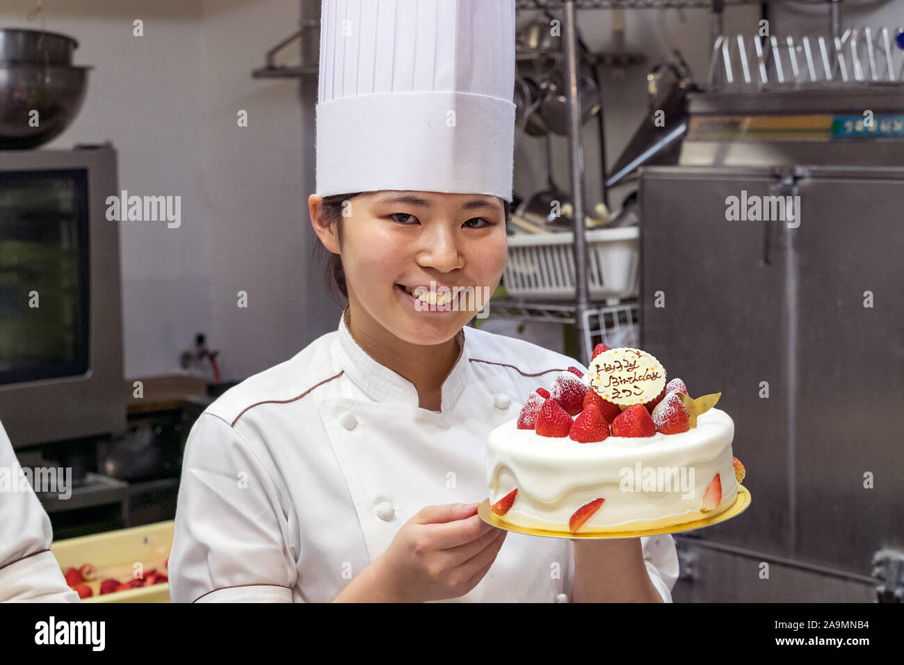 A Japanese female pastry chef showing a birthday cake decorated with