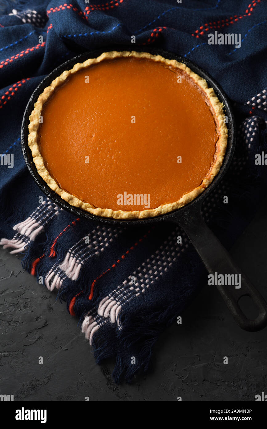 Hygge concept. Homemade pumpkin pie in cast iron pan on dark cozy plaid on black background copy space Stock Photo