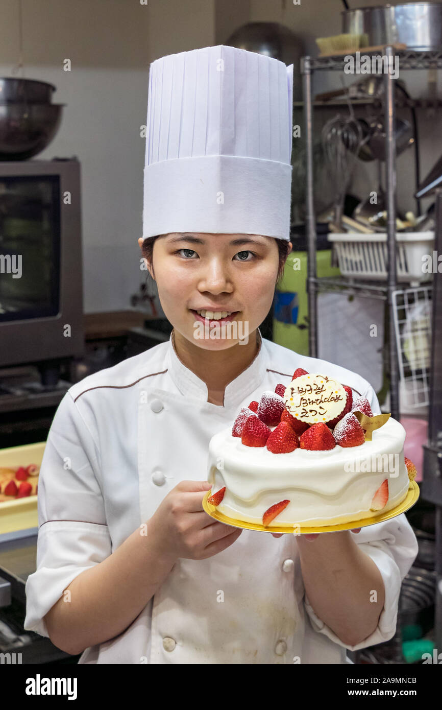 A Japanese female pastry chef showing a birthday cake decorated with