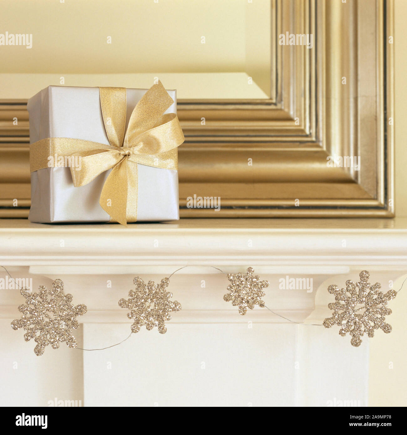 Silver and gold Christmas gift present on mantel with glitter snowflake garland. Beautiful, elegant, fancy holiday home interior decor decorating deco Stock Photo