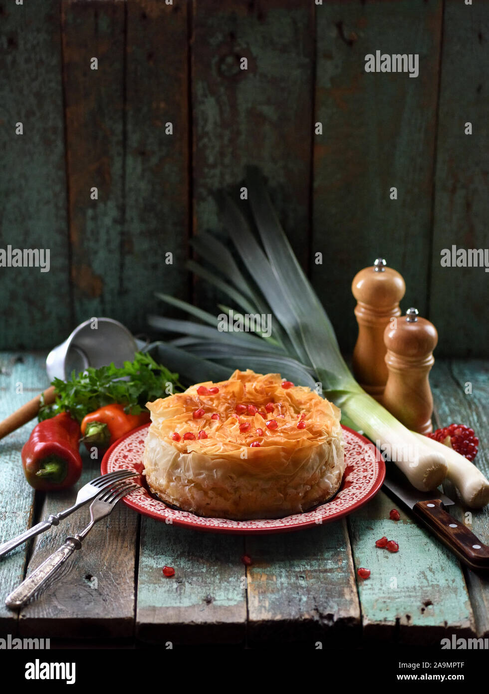 Homemade filo dough pie with raw vegetables and pomegranate seeds on red plate on blue shabby background copy space. Low key still life with natural l Stock Photo