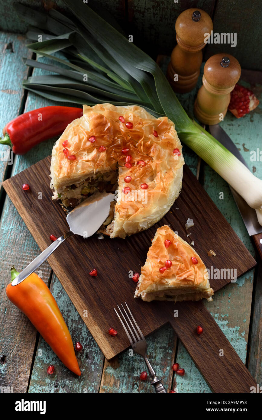 Homemade filo dough pie with raw vegetables and pomegranate seeds on oak board on blue wooden background. Low key still life with natural lighting hig Stock Photo