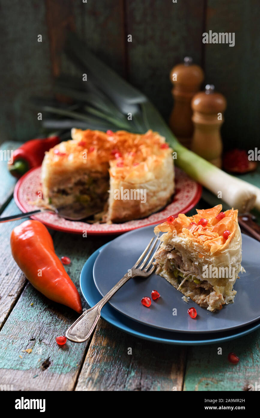 Homemade filo dough pie with chicken and vegetables decorated with pomegranate seeds on blue wooden background copy space. Low key still life with nat Stock Photo