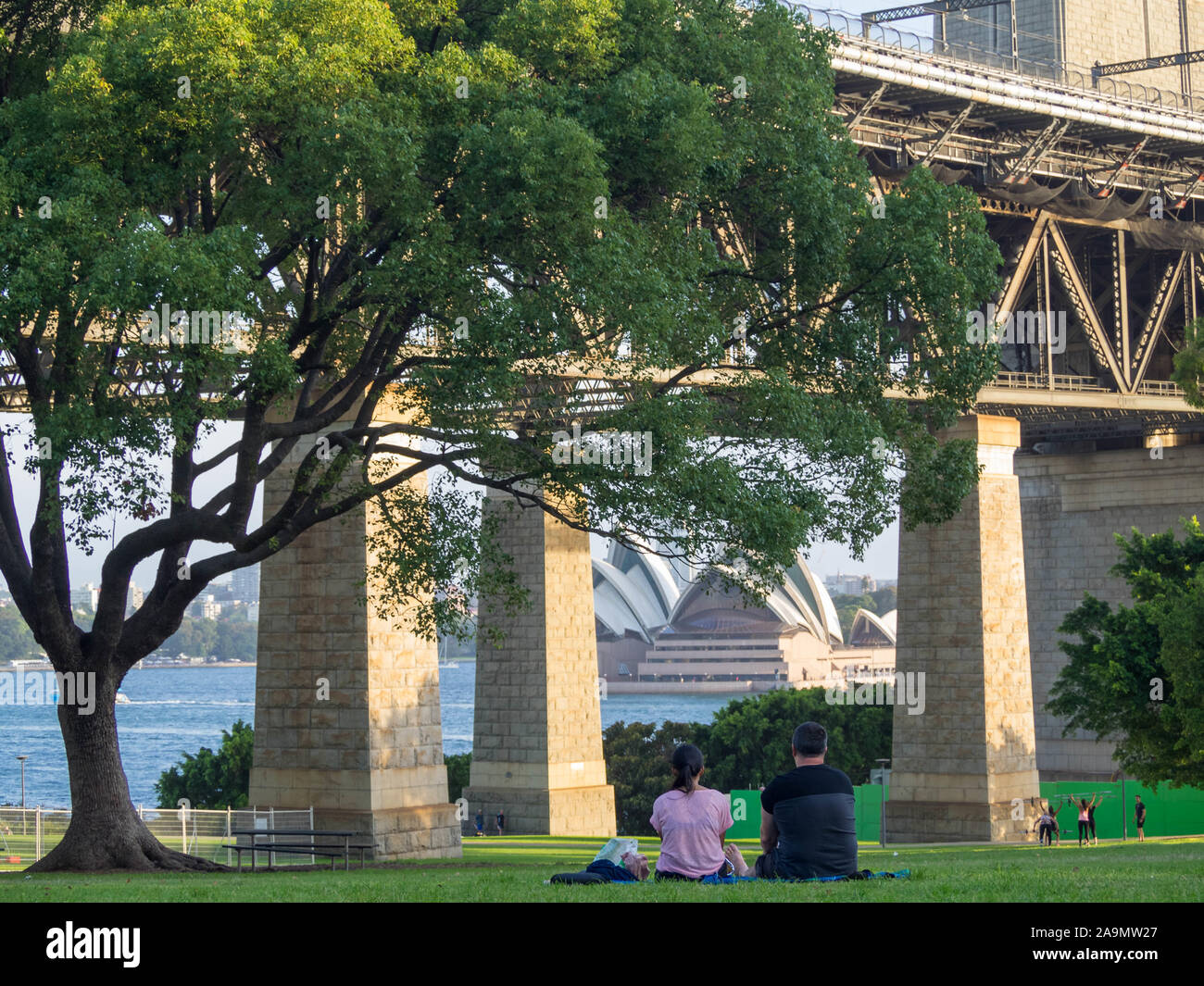 Couple seated in a lawn looking at Sydney Opera House under Harbour Bridge from Milsons Point Stock Photo