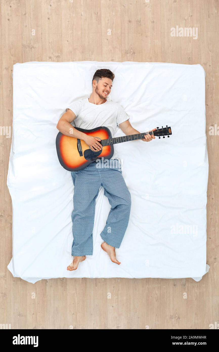 Bedtime Guy Lying On Bed Top View Playing Guitar Cheerful Stock Photo bedtime-guy-lying-on-bed-top-view-playing-guitar-cheerful-stock-photo