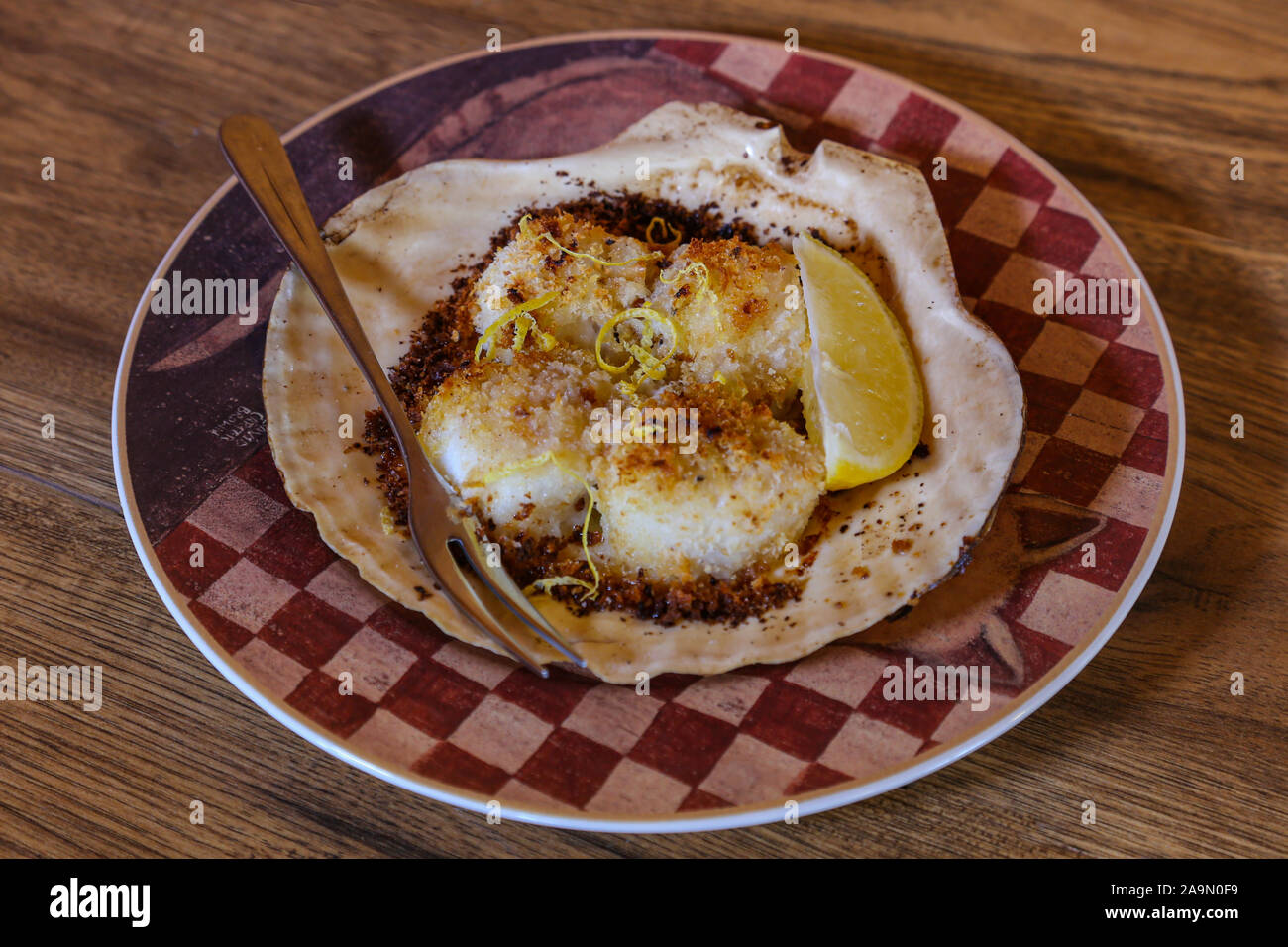 Baked scallops on the half shell served on a plate with seafood fork. Stock Photo