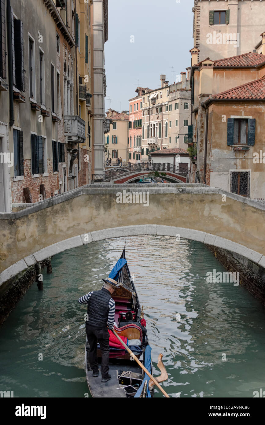 Gondolier with passengers passing under a bridge over a canal Stock Photo