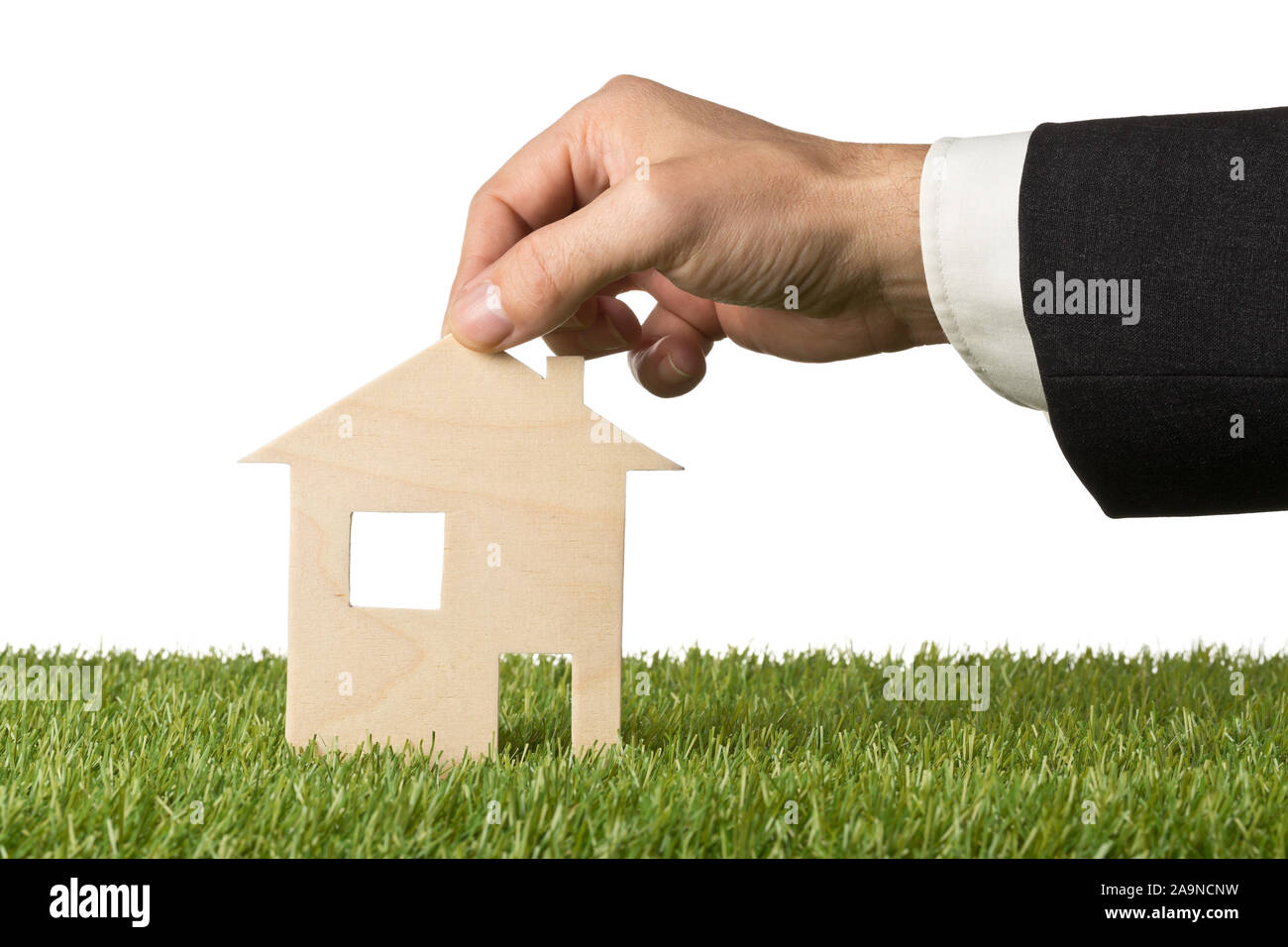 Business man holding little wooden miniature house model on green grass ...