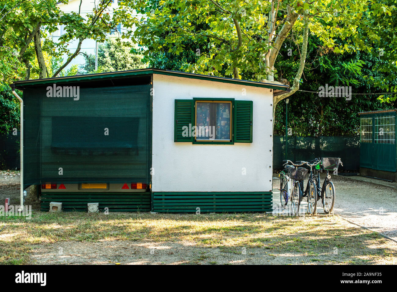 Small white bungalow on campsite. Bikes in front of bungalow. Many trees and alley on camping. Concept for rest and recreation. Travel and accommodati Stock Photo