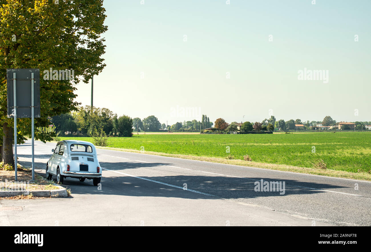 White small vintage car on the street. No people. Asphalt village road in Italy. Travel concept with car. Stock Photo