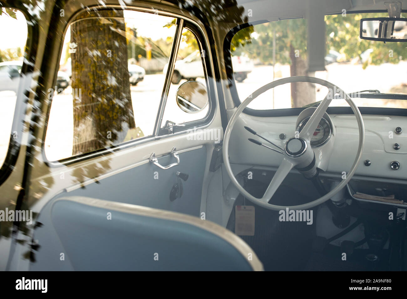 Interior of small white vintage car on the street. No people. White steering wheel. View through the window. Travel concept with car. Stock Photo